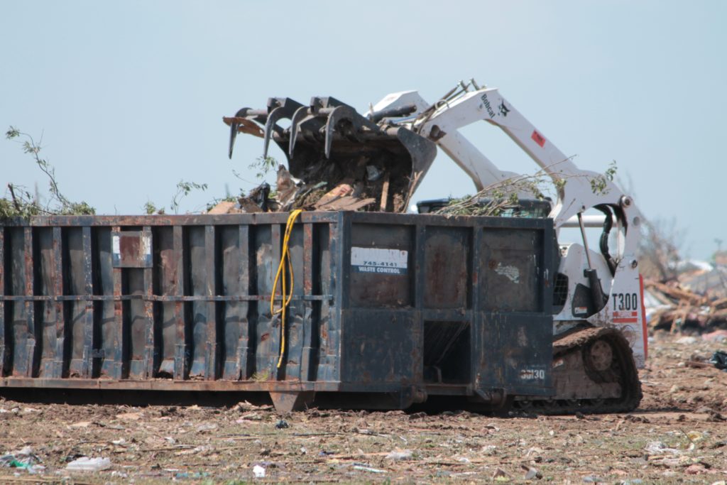 A dumpster being loaded by a skid steer after a natural disaster