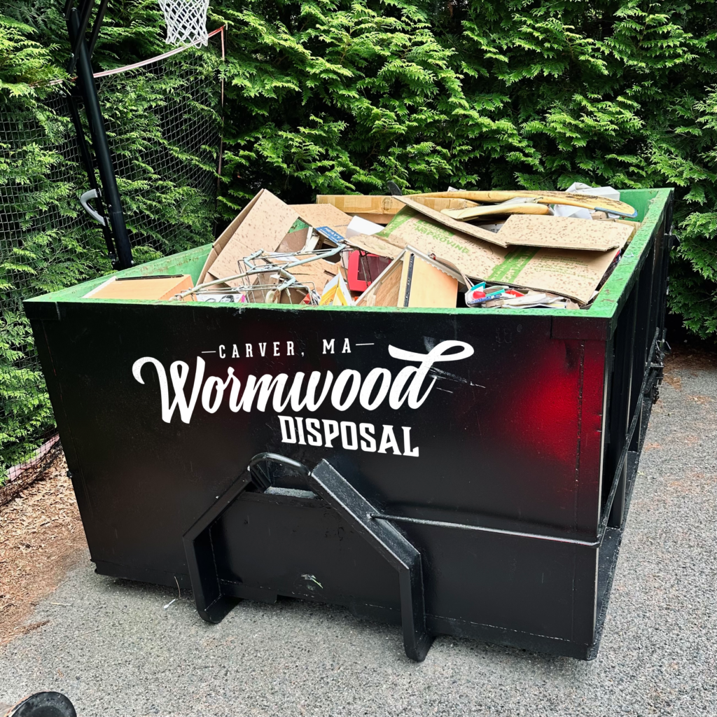 Black 12 Yard dumpster with Wormwood DIsposal logo full of cardboard and debris in a driveway