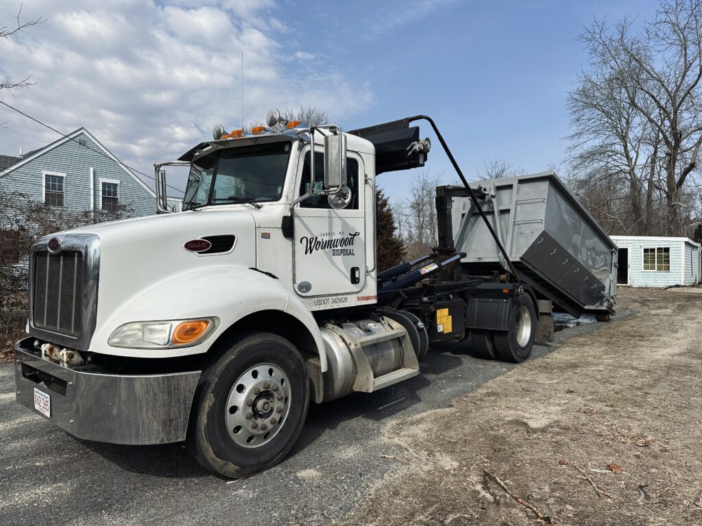 Wormwood Disposal truck loading a dumpster in a driveway located in Wareham Massachusetts