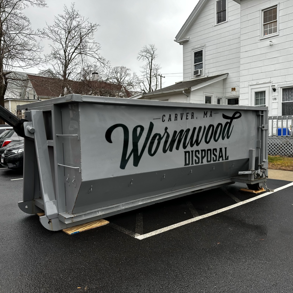 A gray 20 yard dumpster with a wormwood disposal logo in a parking space