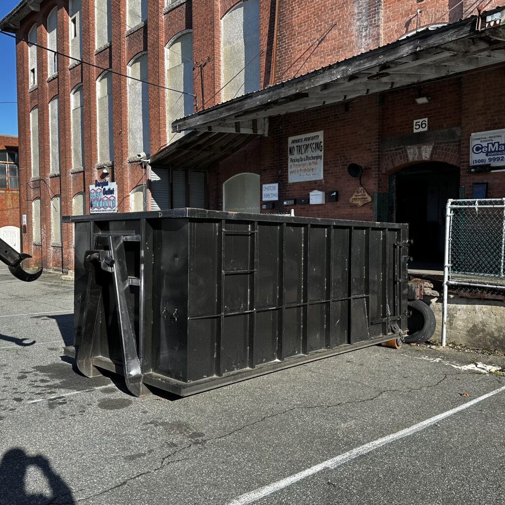 Black Wormwood Disposal dumpster placed in front of a loading dock in New Bedford