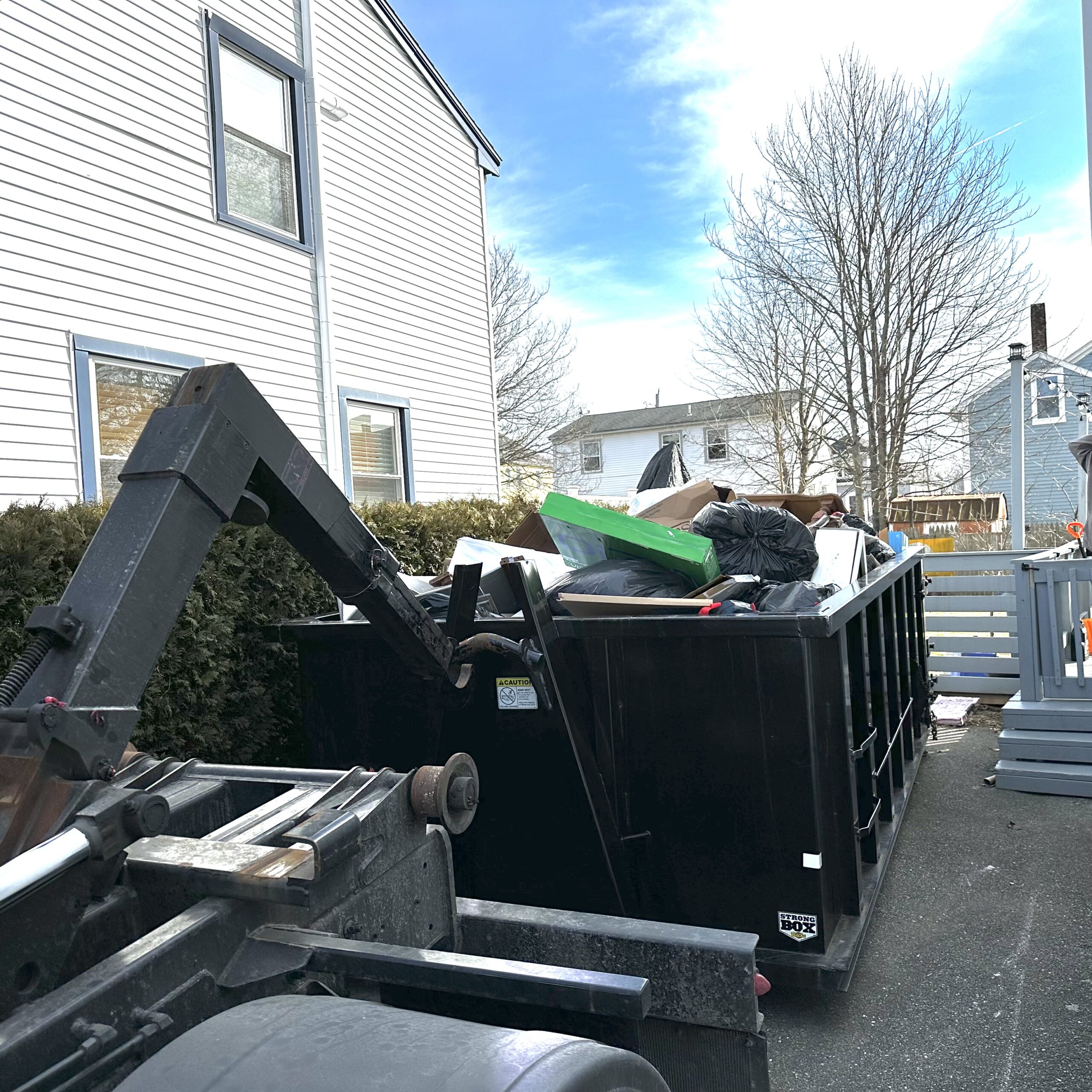 a black 15 yard dumpster full of junk in a narrow driveway