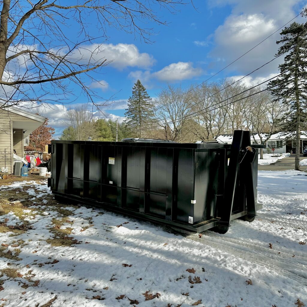 Black 15 yard dumpster sitting on snow covered grass in taunton ma